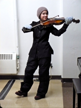 Musician in concert attire playing viola with thick snow gloves and winter hat